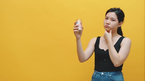 Sad Pensive Young Asian Woman Holding Money Jar with Savings. Low Income and Big Expenditure Concept