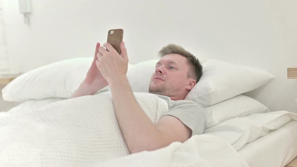 Man Using Smart Phone in Bed