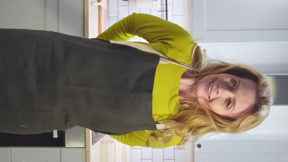 Vertical View of Attractive Mature Female Adjusting Apron in Kitchen