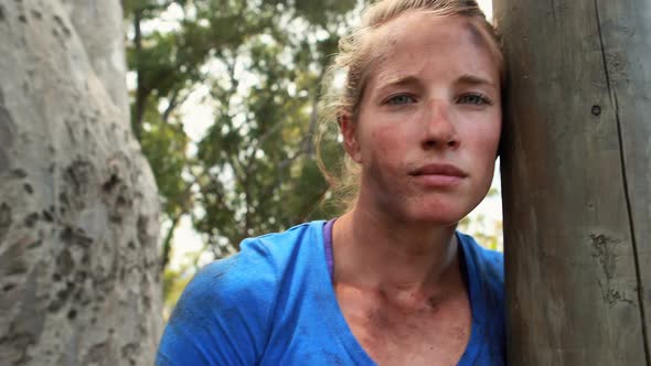 Portrait of fit woman leaning on wooden pole during obstacle course