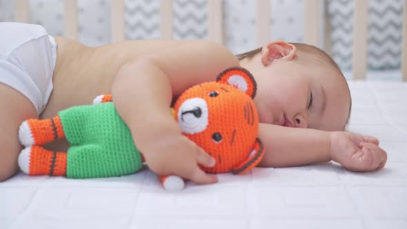 Toddler 12-17 months old sleeps in bed hugging a knitted tiger toy. Close up