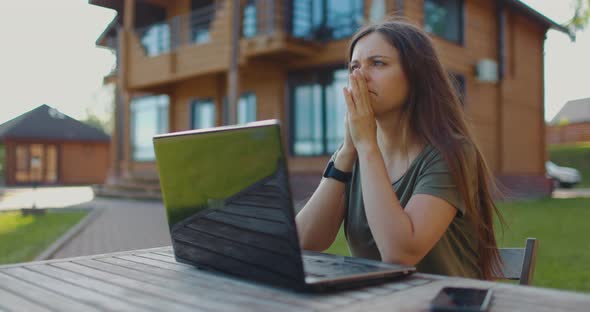 Focused Young Girl Looks at Laptop Monitor While Sitting at Table in Courtyard of Country House