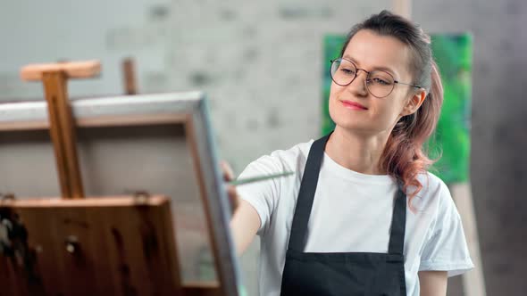 Smiling Young Woman in Apron Enjoying Drawing Picture at Art Studio Medium Closeup