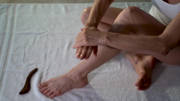 Overhead view of mature woman rubbing coconut oil on her hands and then applying to her leg.