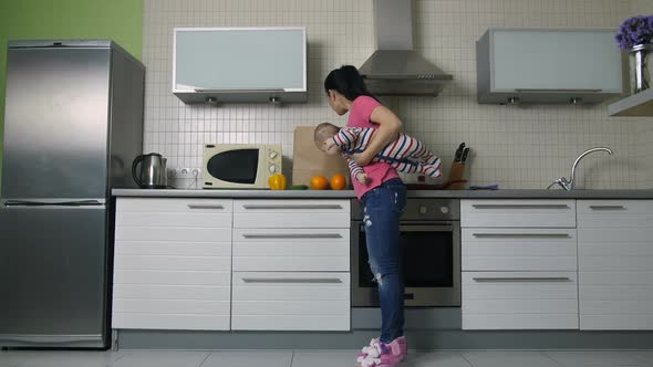 Mother with Baby Unloading Shopping Bag in Kitchen