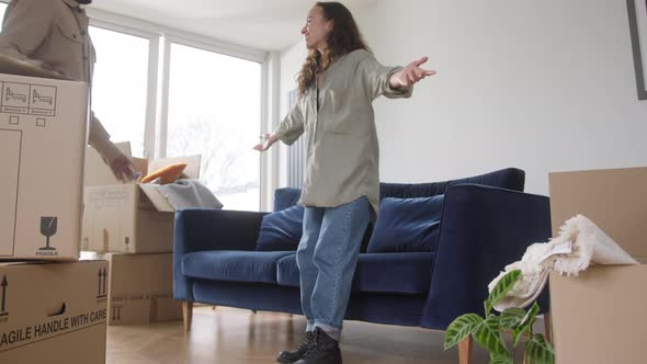 Young Couple In New Home Sitting On Sofa In Lounge On Moving Day Surrounded by Removal Boxes