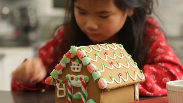 Closeup of young girl decorating gingerbread house for Christmas alt