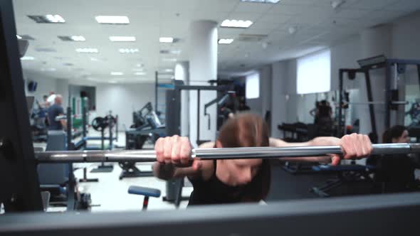 Beautiful woman with strong hands raises barbell in a fitness club