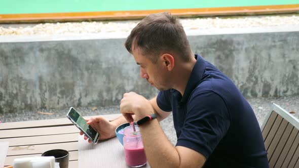 Young Handsome Man Watch News Feed in Phone Drink Pink Healthy Fruit Smoothie