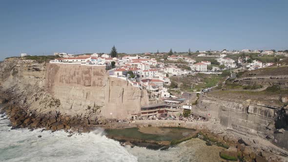 Pedestal dolly in shot capturing natural swimming pool and clifftop village in Azenhas do Mar.