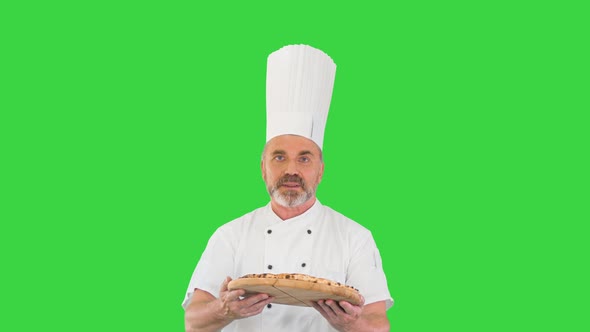 Attractive Cook with a Pizza in Hands Walking and Talking To Camera on a Green Screen, Chroma Key.