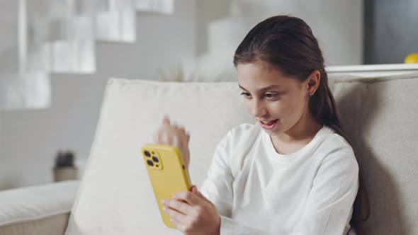 Female Teen Reading Good News on Mobile on Couch