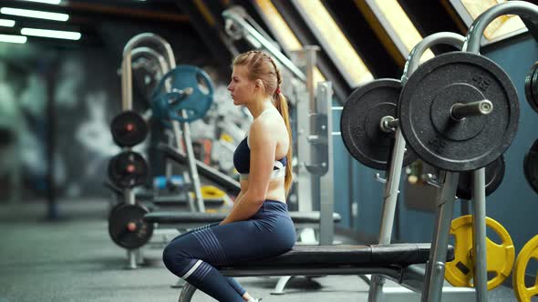 Woman sitting on bench for barbell lifting in gym