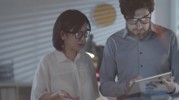 Colleagues with Tablet Discussing Work in Office in Evening