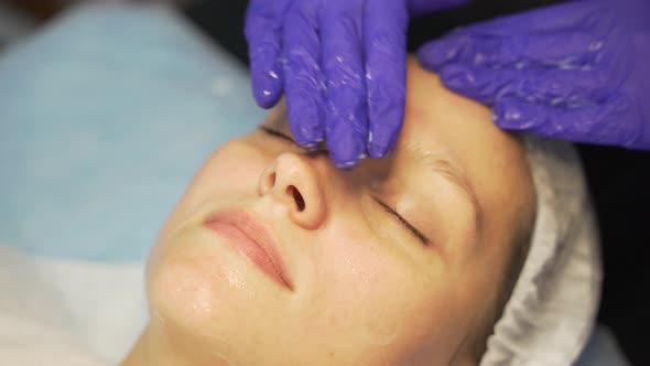 Cosmetologist Applies Transparent Composition to Woman's Face with Circular Movements Before