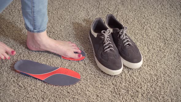 Female Feet Standing on the Orthotics Near Sneakers