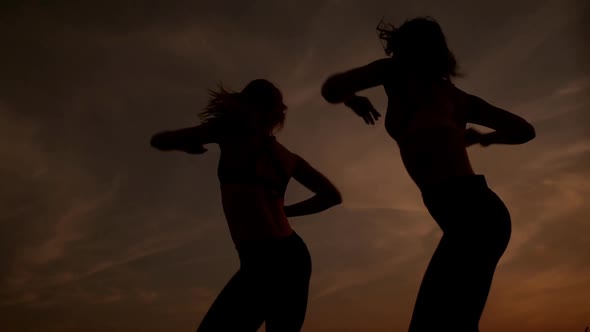 Silhouettes of Two Beautiful Girls Dancing Zumba in Field at Sunrise