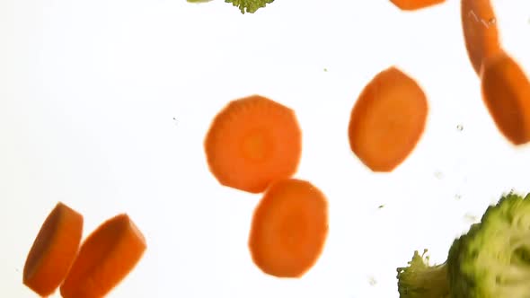 Cut slices of carrot and broccoli in water over white bacjground