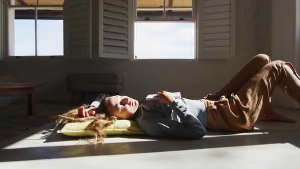 Caucasian woman lying on floor holding book and sleeping in sunny cottage living room