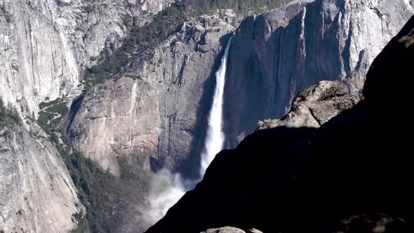 High Yosemite falls cascading drop from behind rock cliff wall, Dolly left shot