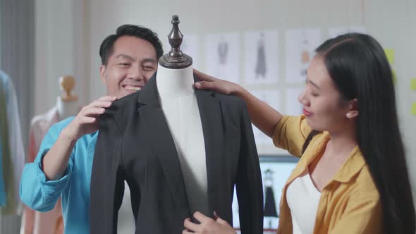 Asian Male And Female Designers Helping Each Other Wearing Business Jacket On A Mannequin