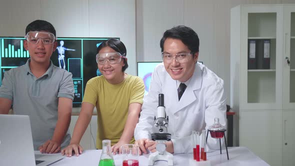 Asian Boy And Girl Learning Science Experiment In Laboratory With Teacher, They Smile To Camera