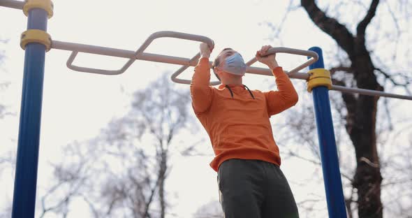 Man Pulls Up on the Bar Outdoor in a Surgical Mask