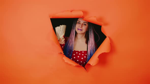 Bright Woman with Money Sticks Out of Hole of Orange Background