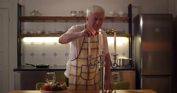 Senior Man in Apron Lighting Candles Preparing Romantic Dinner for Wife