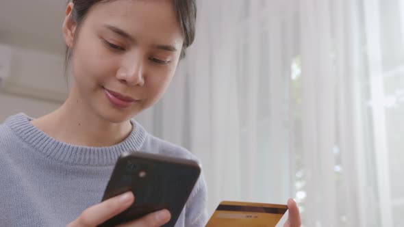 Young Asian woman holding smartphone and credit card with paying for shopping online.