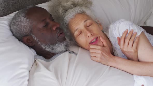 Mixed race senior couple sleeping together on the bed at home