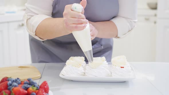 a Female Chef Adds Cream From a Pastry Bag to Anna Pavlova Cakes in the Kitchen