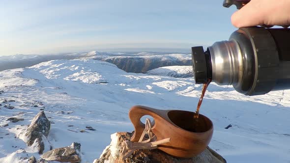 Person pouring coffee to wooden mug at idyllic snow covered mountains landscape - Slow motion