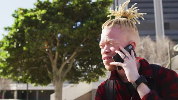 Happy albino african american man with dreadlocks in park talking on smartphone