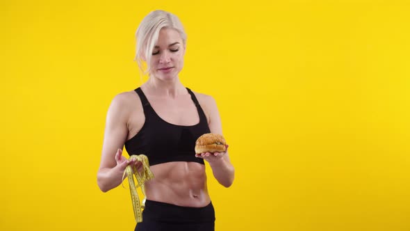 Woman on Yellow Background Hold Measuring Tape and Burger in Her Hands She Weighs Them and Stop the