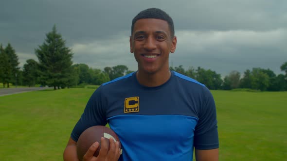 Handsome Sporty Fit Black American Football Player with Ball Smiling Outdoors