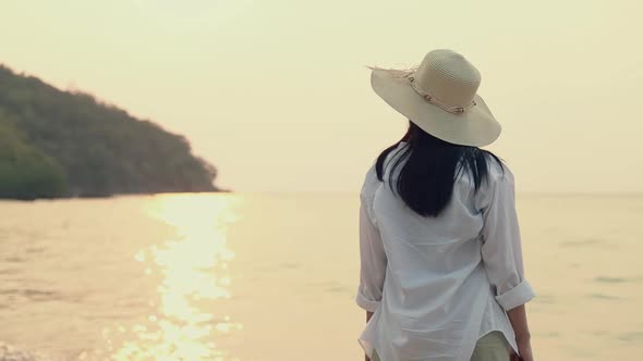 Portrait of attractive Asian woman wearing fedora hat standing on the beach looking at sea view.