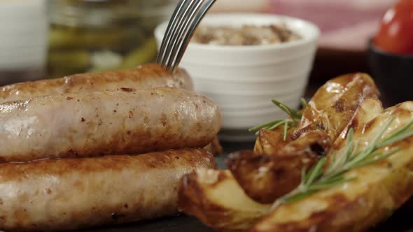 Taking Smoked Sausages with Fork Fried Potatoes and Sauce Closeup