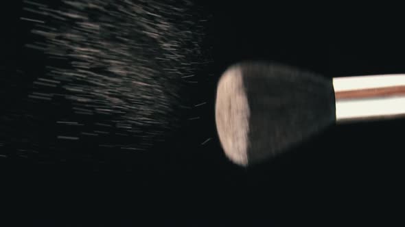 Cosmetic Powder for the Face is Poured From a Brush on a Black Background