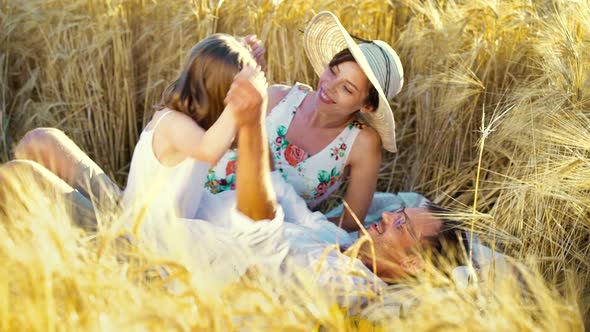 Happy family with little daughter playing in wheat field in summer