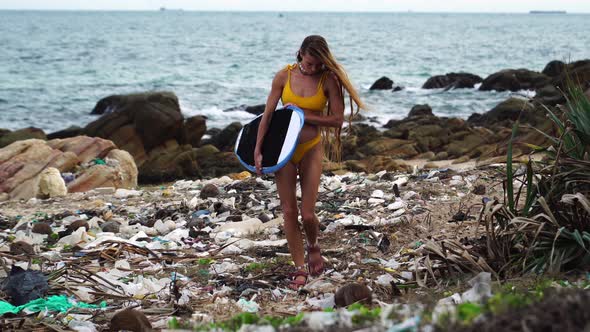 Caucasian young woman surfer walking on polluted beach wearing sandals over plastic bag waste garbag