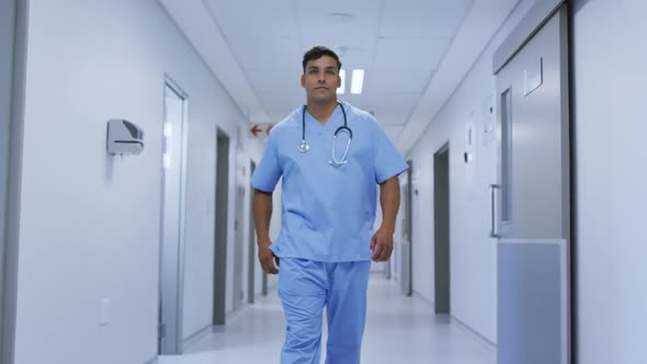 Portrait of smiling mixed race male doctor wearing scrubs walking in hospital corridor