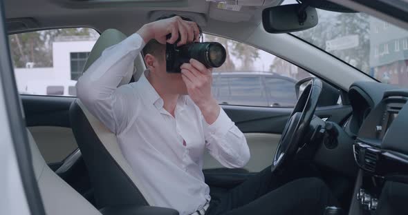 Man with Camera Sitting Inside Car and Making Photo with Professional Camera Private Detective or