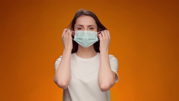 Young Woman Takes Off Medical Mask and Smiles Against Yellow Background