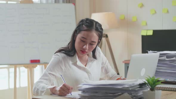 Asian Woman Looking At Laptop And Taking Note While Working With Documents At The Office