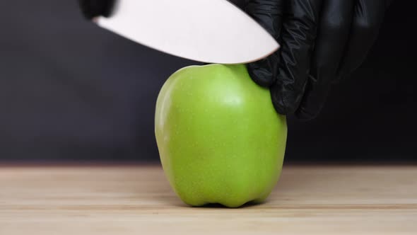 Cuts an apple in half with a knife on black background