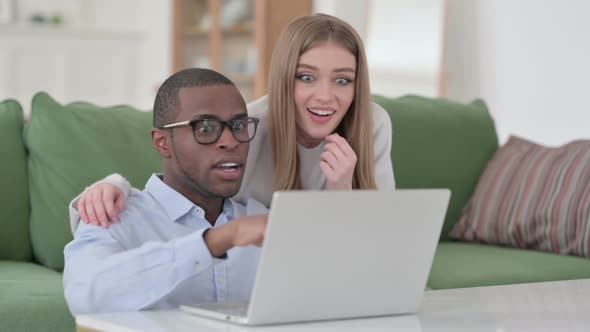 Mixed Race Couple Celebrating Success While Using Laptop at Home