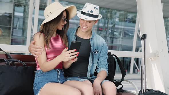 Travel. Couple Using Phone And Sitting Near Airport Terminal