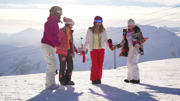 Four Caucasian Females Holding Each Other Hands and Smiling Wearing Ski Costumes and Masks at