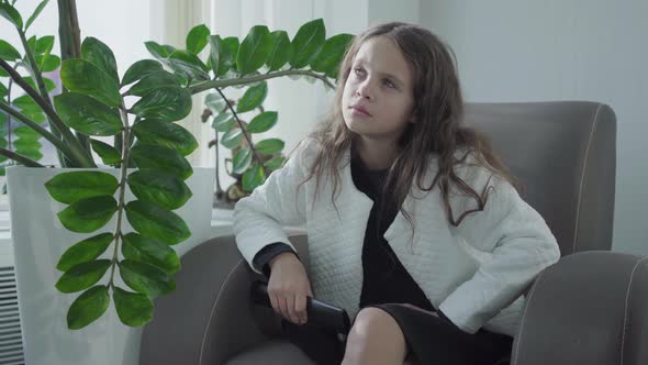 Little Pretty Caucasian Girl with Curly Hair Watching TV in the VIP Waiting Room at the Airport